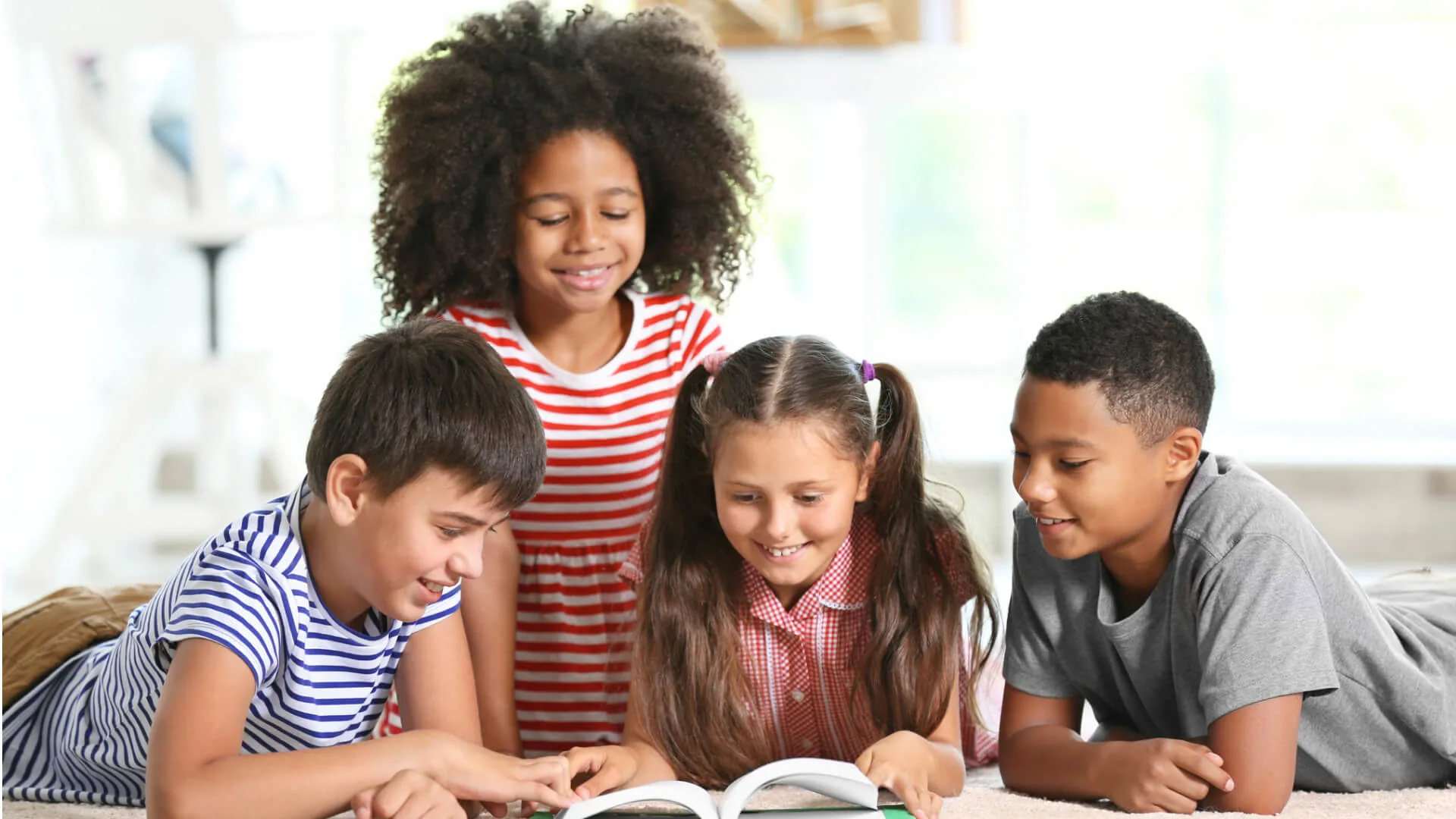 Four children gathered together, smiling as they read a book